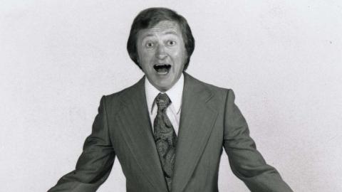 A 1970s publicity shot of Graham Kennedy wearing a suit and exclaiming at the camera.