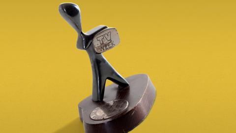 A TV Week Logie Award, made up of a small silver statuette in the shape of a man holding a television. The statuette sits on a round wooden base with a metal disc with words engraved on it. 