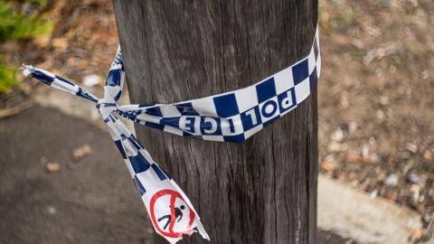 A section of a telegraph pole on a sidewalk with some blue and white chequered police tape tied around it.