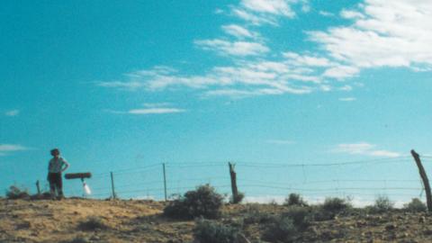 Bronwyn Murphy photographed near fence from a distance with blue sky in the background during filming of Rabbit Proof Fence