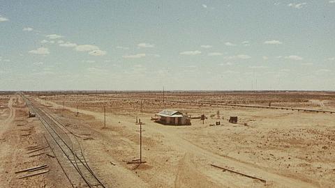 An aerial shot of a hotel and railway line in a vast expanse of outback, in a scene from the 1971 film Wake in Fright