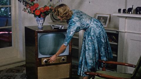 1950s image of a woman turning on a television set in her living room.