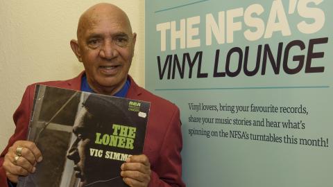 Vic Simms holding a copy of his record The Loner in front of the Vinyl Lounge banner