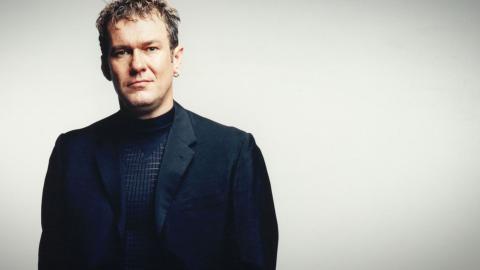 Jimmy Barnes wearing a black suit and shirt and looking directly at camera. Photographed from waist up.