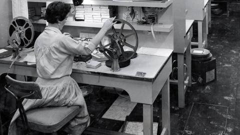 A woman sitting with her back to the camera winding a film reel.