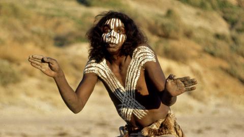 David Gulpilil dancing on the set of Storm Boy. He is wearing body paint on his face and torso.