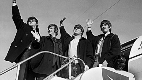 The Beatles (from left to right: Paul McCartney, Ringo Starr, John Lennon, George Harrison) wave to crowds in Sydney as they prepare to board a plane to New Zealand in June 1964.