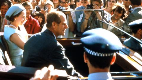 Queen Elizabeth and Prince Philip riding in the back of a car in Sydney in 1973, surrounded by members of the public and photographers. 