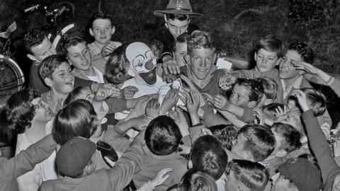 Bobo the clown is surrounded by a crowd of children reaching out to touch him