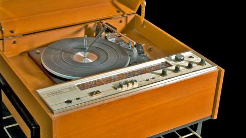 An HMV branded radiogram from the early 1970s. It features a turntable for vinyl records and an AM radio receiver encased in a tan-coloured wood cabinet. 