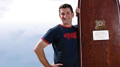 Warren Brown standing next to a large wooden surfboard