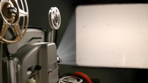 Old film projector shining light onto a rectangular white screen in a dark room