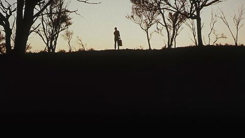 A still image from Wake in Fright shows a silhouetted man surrounded by trees