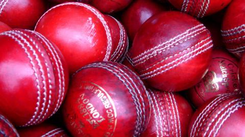 A close up of a collection of new and used red cricket balls inside a basket.